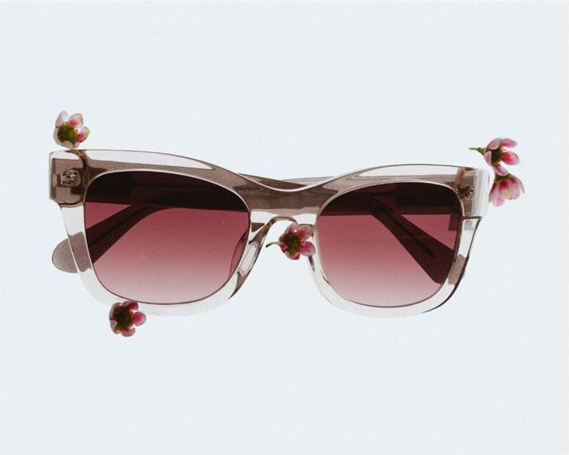A pair of translucent sunglasses with reddish lenses, decorated with small pink flowers against a white background.