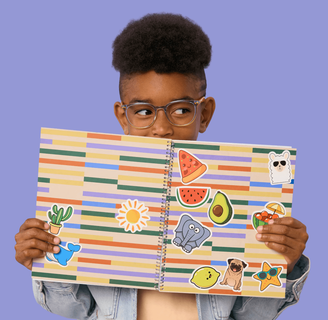 A young boy with glasses peeks over an open, sticker-covered notebook against a purple background.