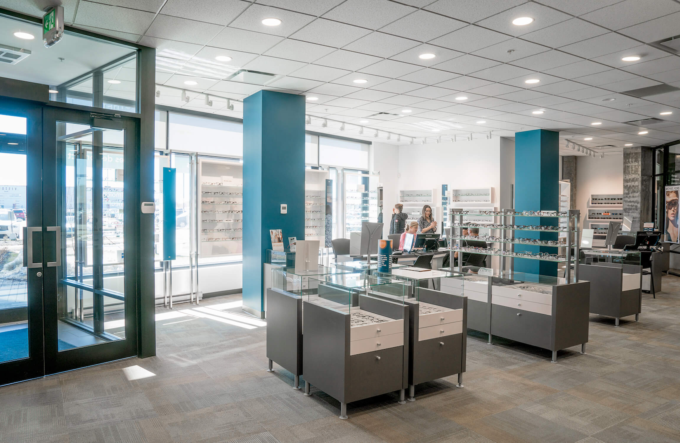 Modern eyewear store interior with display cases and people at the counter.