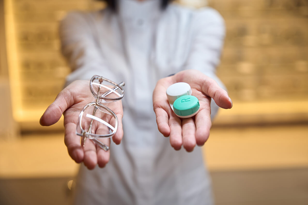 Optometrist holding eyeglasses in one hand and a contact lens case in the other.