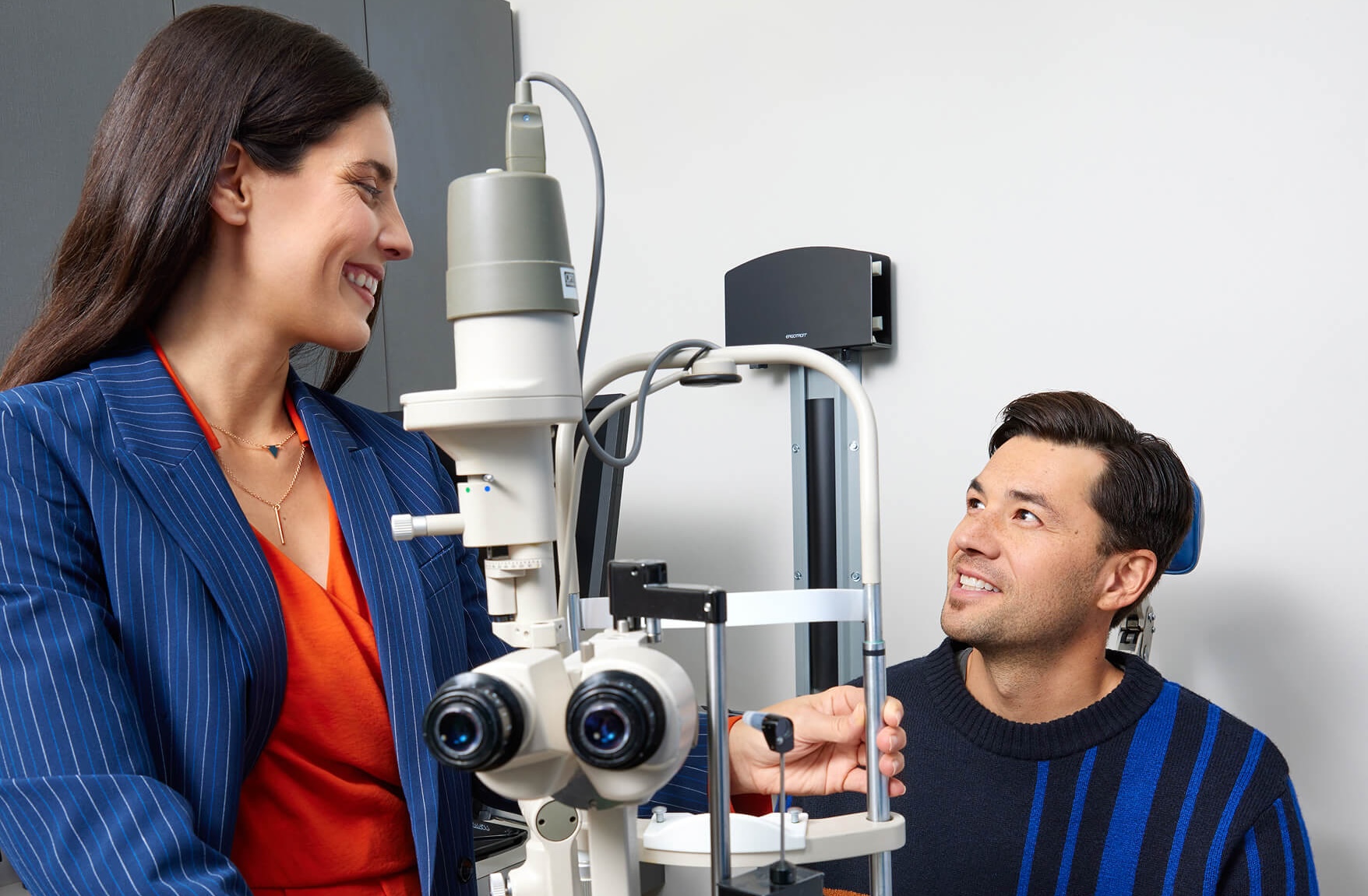 Woman and man smiling near an eye examination machine in a clinic.