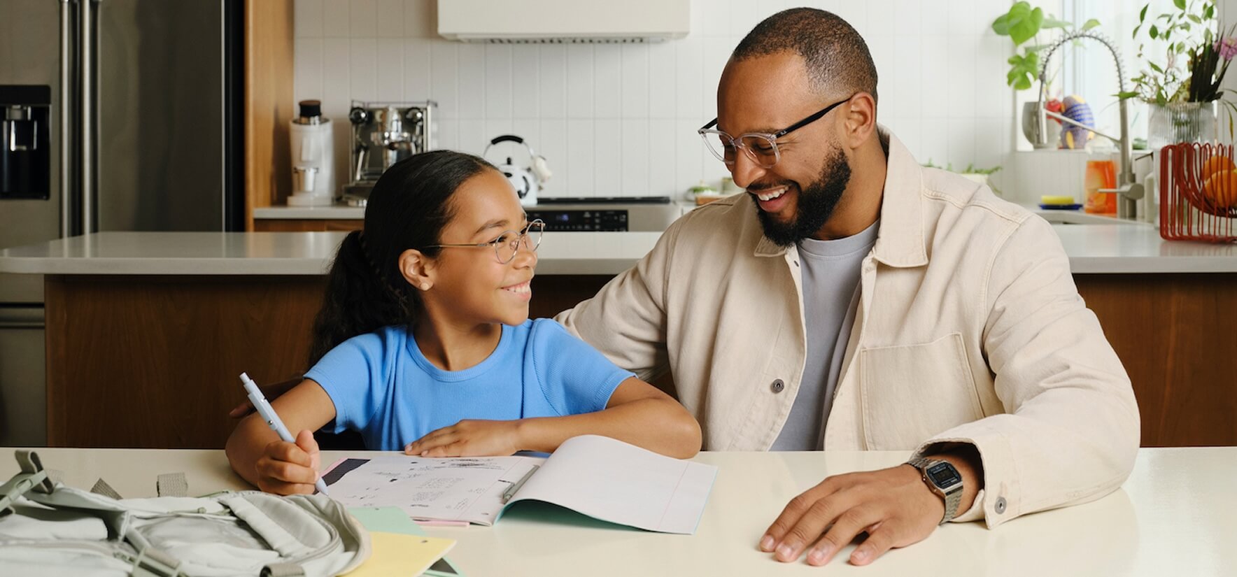 A man and child smiling while doing homework at a kitchen table.