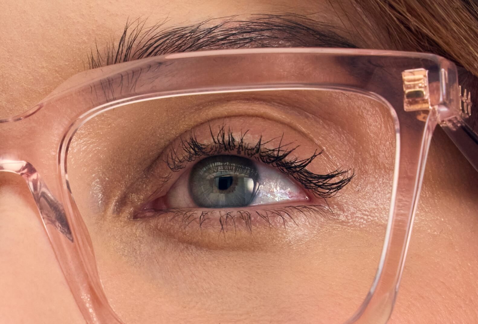 A close-up of a person's eye looking through a pair of translucent pink glasses.
