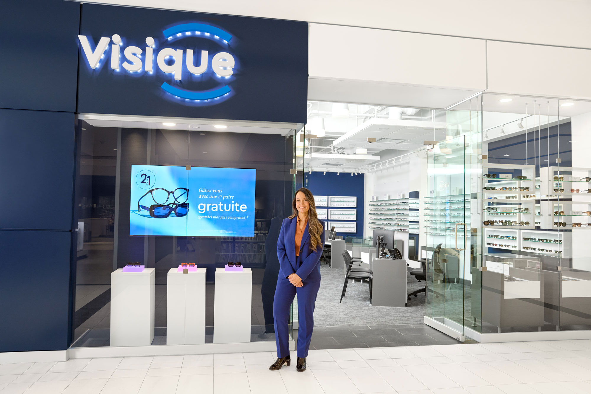 Person in blue suit standing outside eyewear store and clinic 'Visique' with display window.