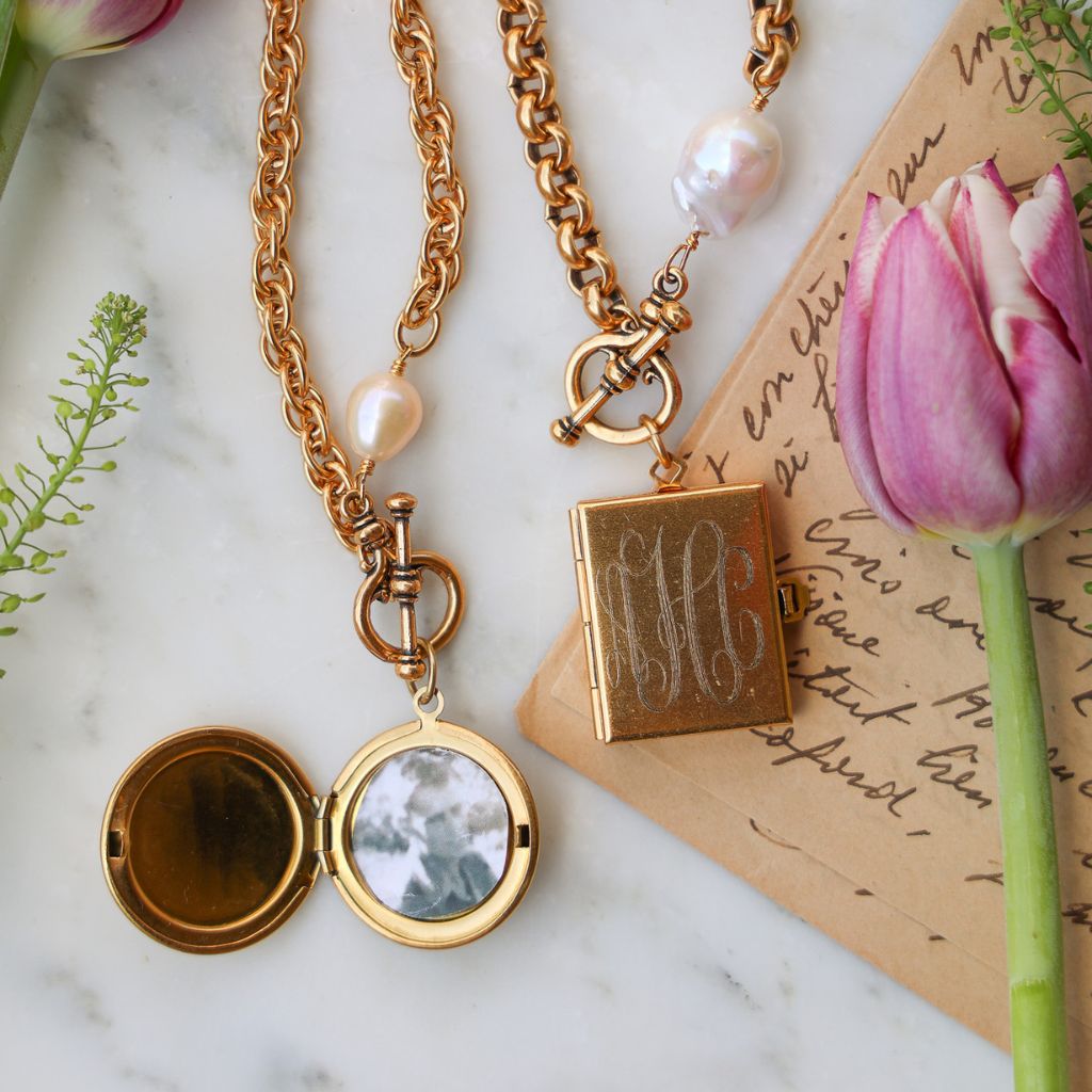 Two gold locket necklaces with pearls are displayed with a pink tulip and a handwritten letter.