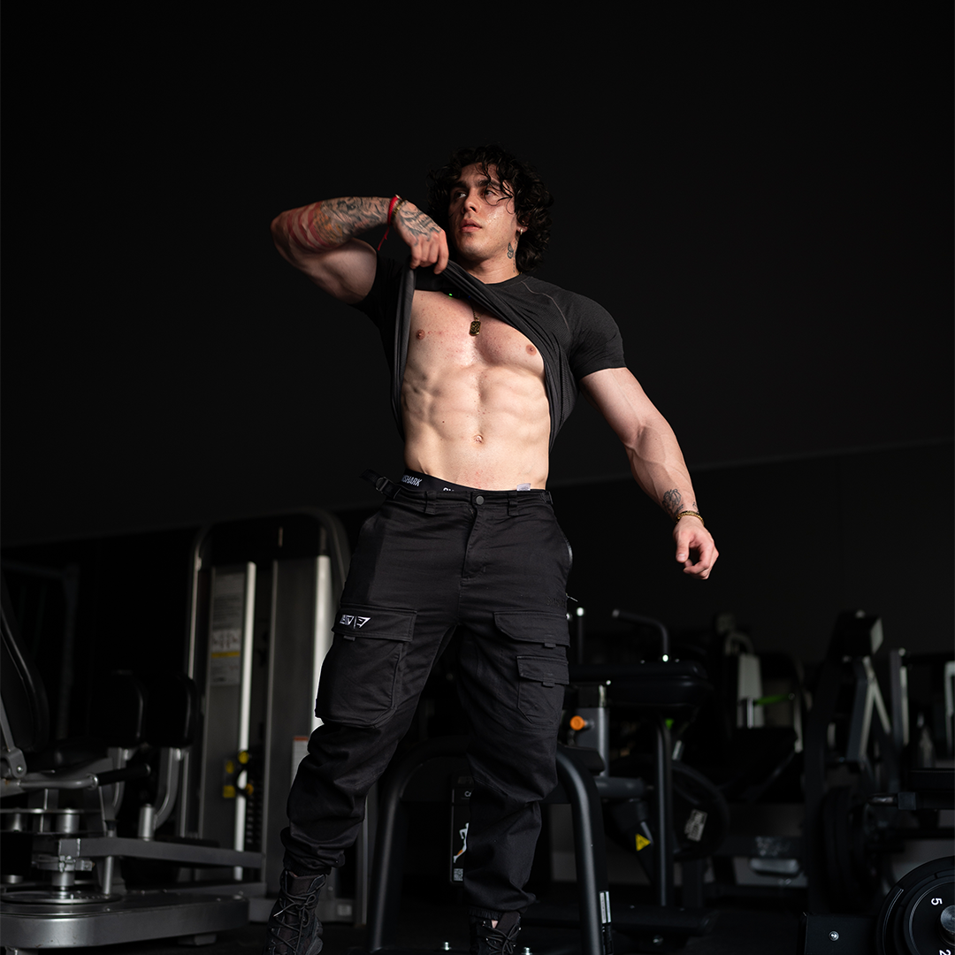 Person in gym lifting shirt to reveal muscular abs.
