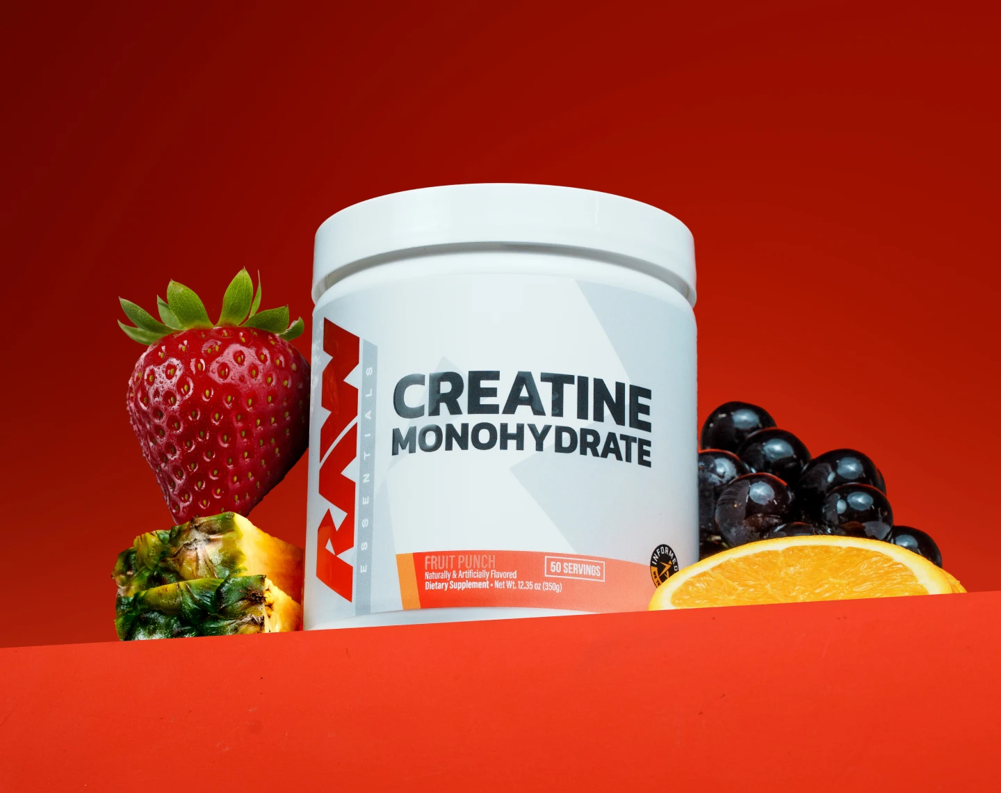 A white tub of RAW Creatine Monohydrate, fruit punch flavor, is surrounded by various fruits on a red background.