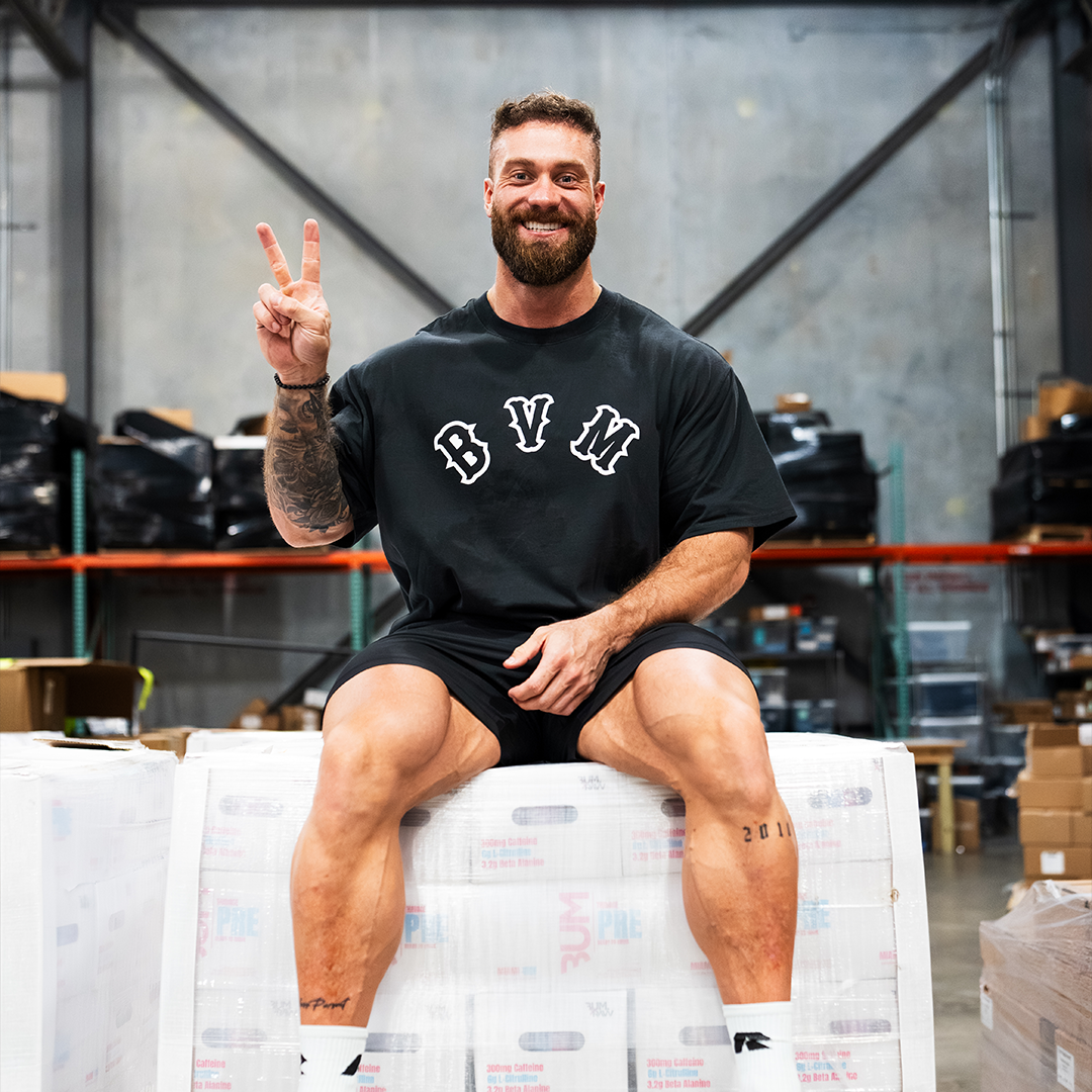 Man sitting on boxes in a warehouse, smiling and showing a peace sign.