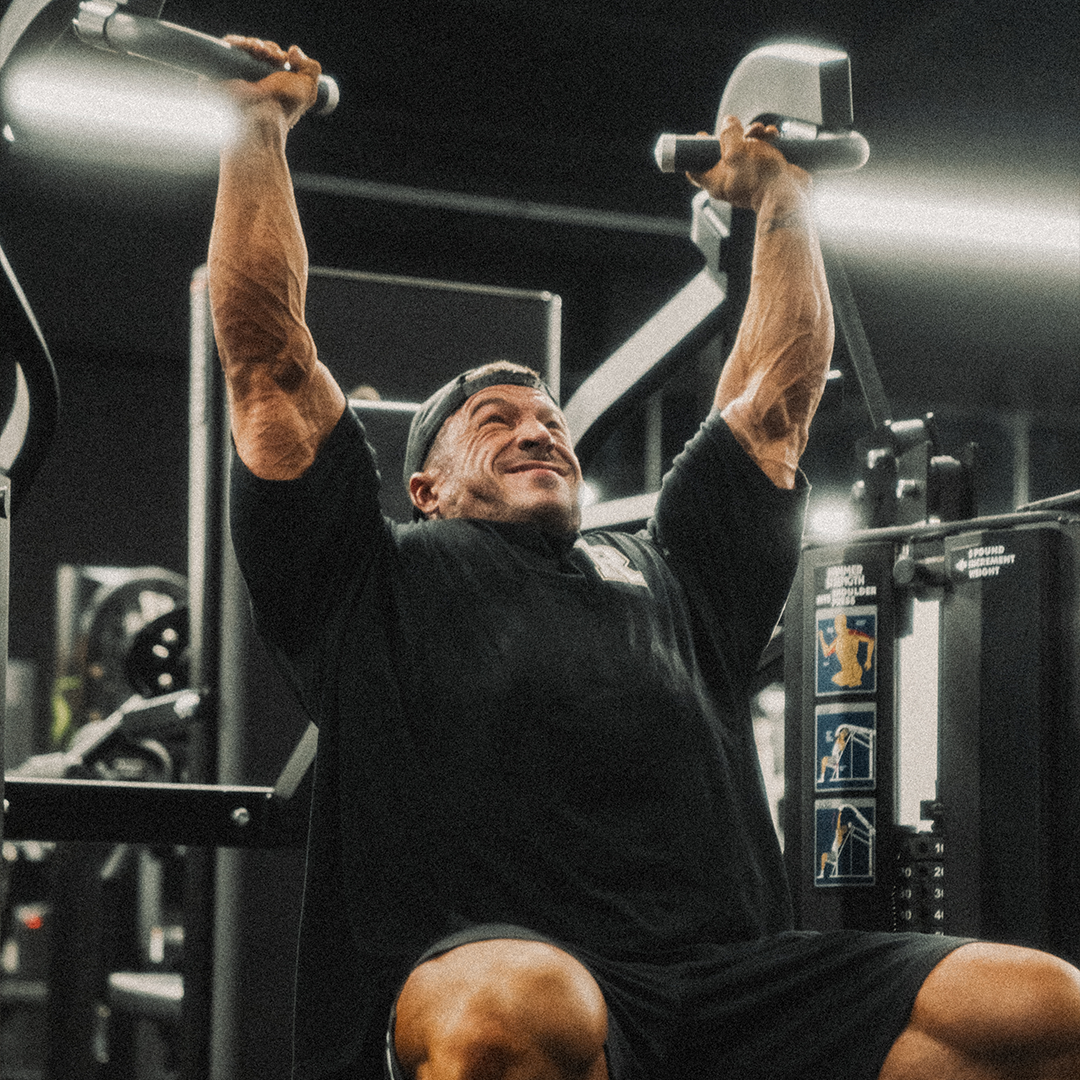 Man lifting weights on a shoulder press machine in a gym.