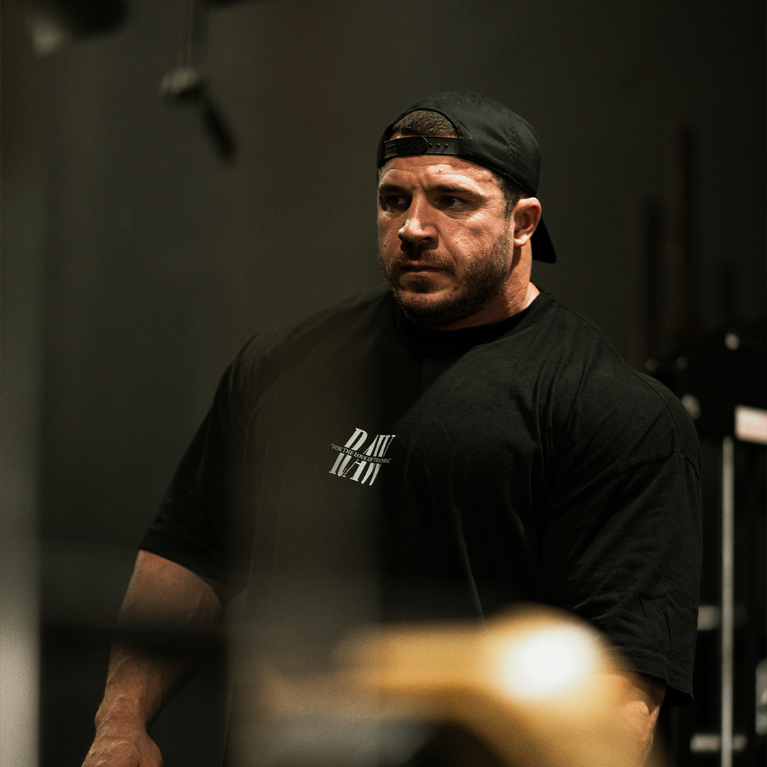 Man in a black shirt and cap, standing in a gym.