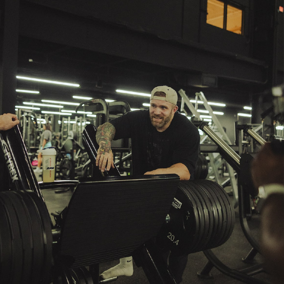 Man with tattoos smiling in a gym near weightlifting equipment.