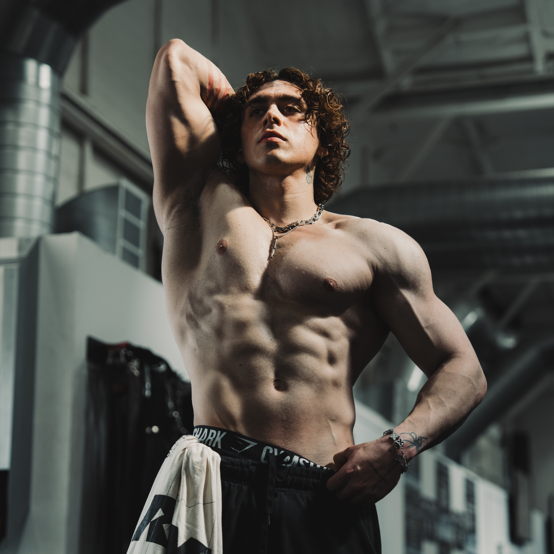 Muscular person posing shirtless in a gym setting.