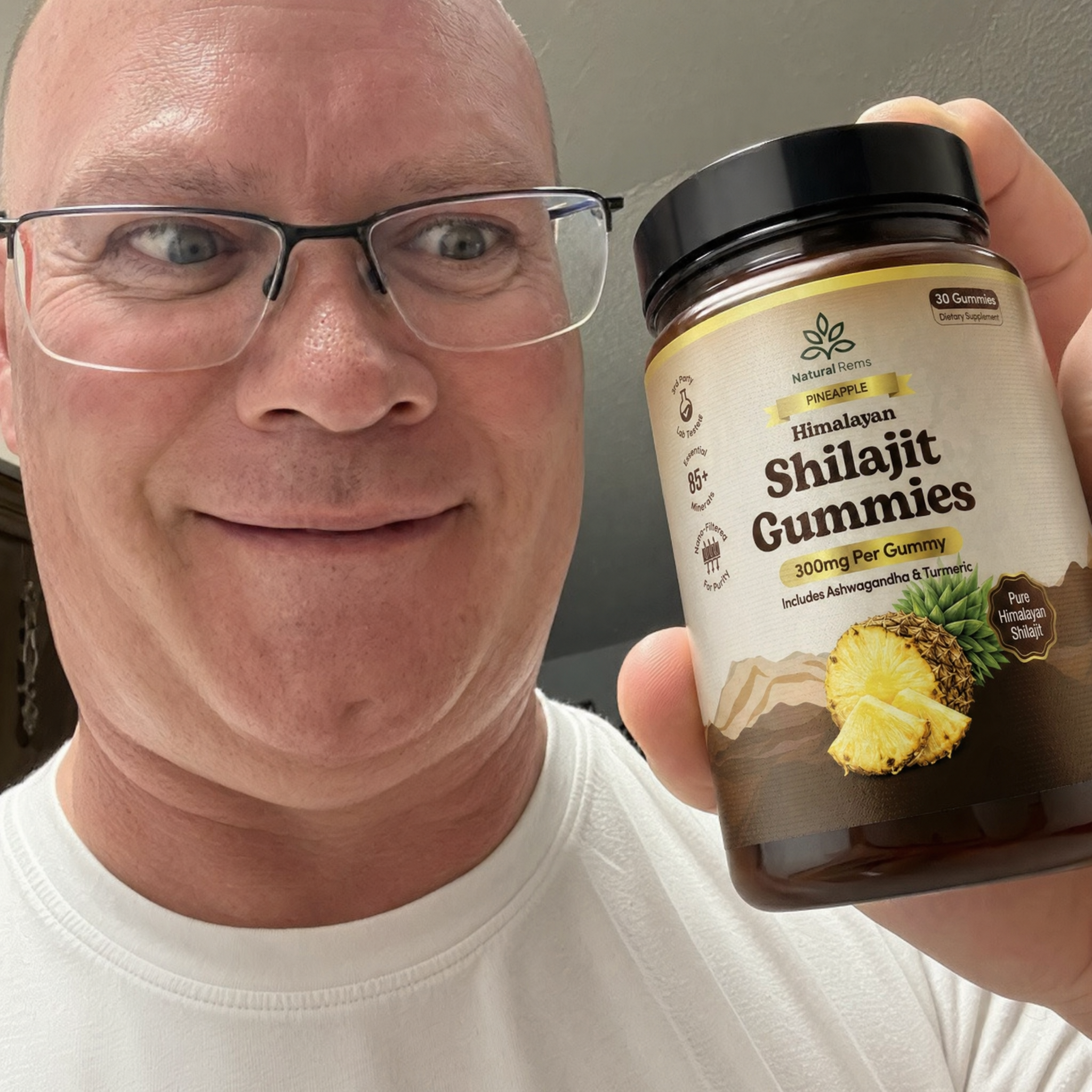 A smiling man wearing glasses holds up a bottle of Himalayan Shilajit Gummies.