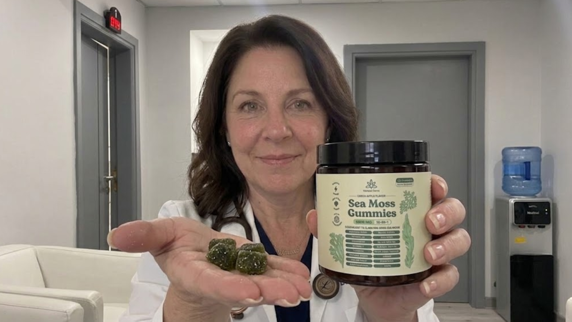 A woman in a white coat holds a jar of Sea Moss Gummies and a few gummies.