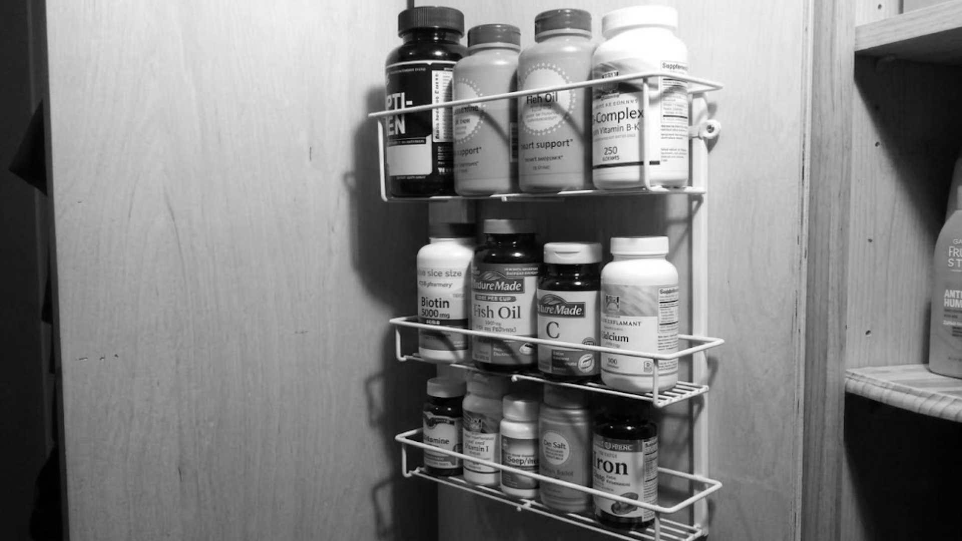 A black and white photo of a wire rack filled with bottles of vitamins and supplements.