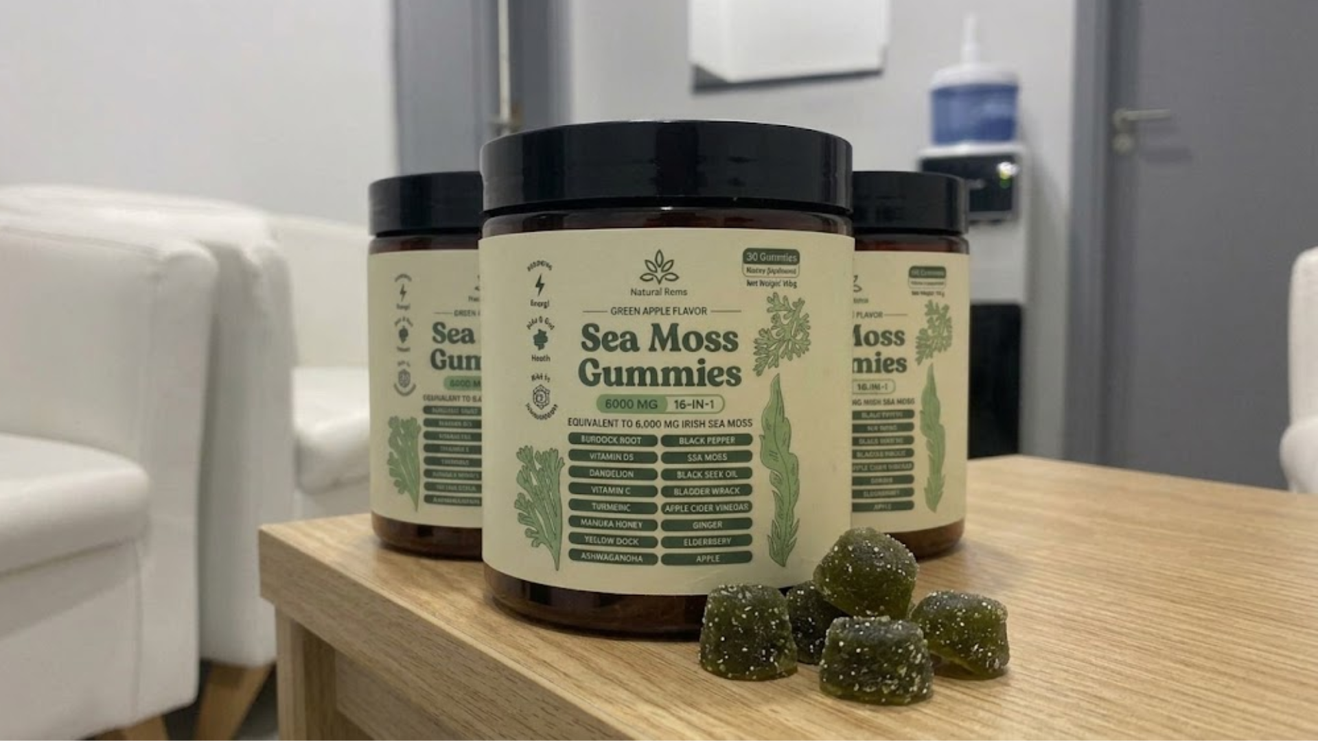Three jars of Sea Moss Gummies sit on a wooden table with several loose gummies in front.