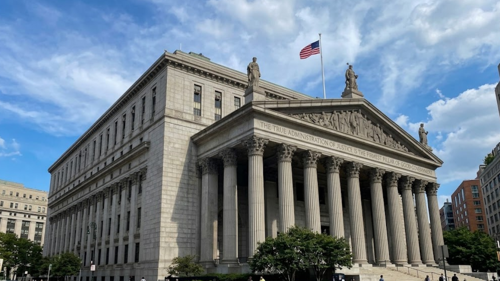 A low-angle shot of a grand stone courthouse with columns and an American flag against a blue sky.