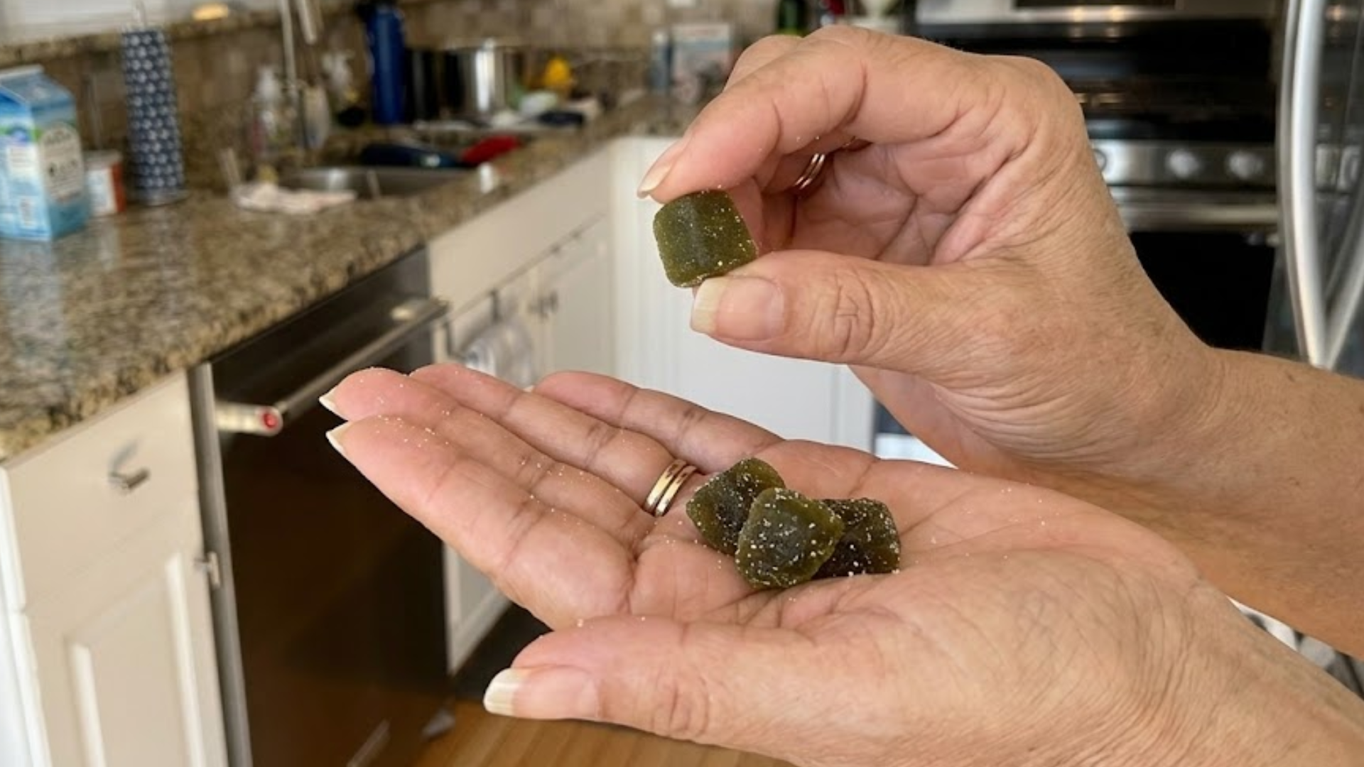 A person's hands holding several dark, sugar-coated gummies in a kitchen.