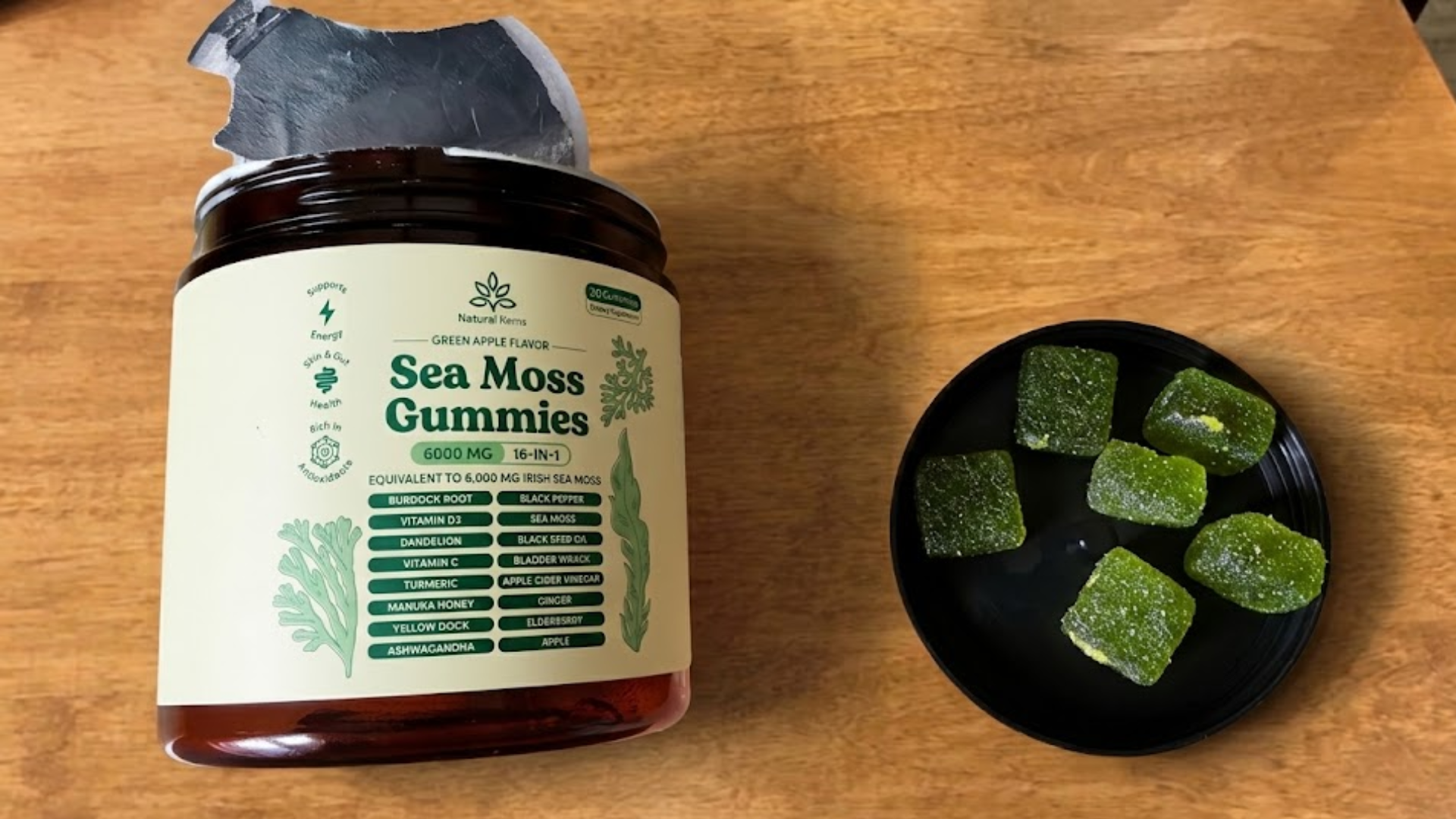 An open jar of Sea Moss Gummies sits on a wooden table next to a plate of green gummies.