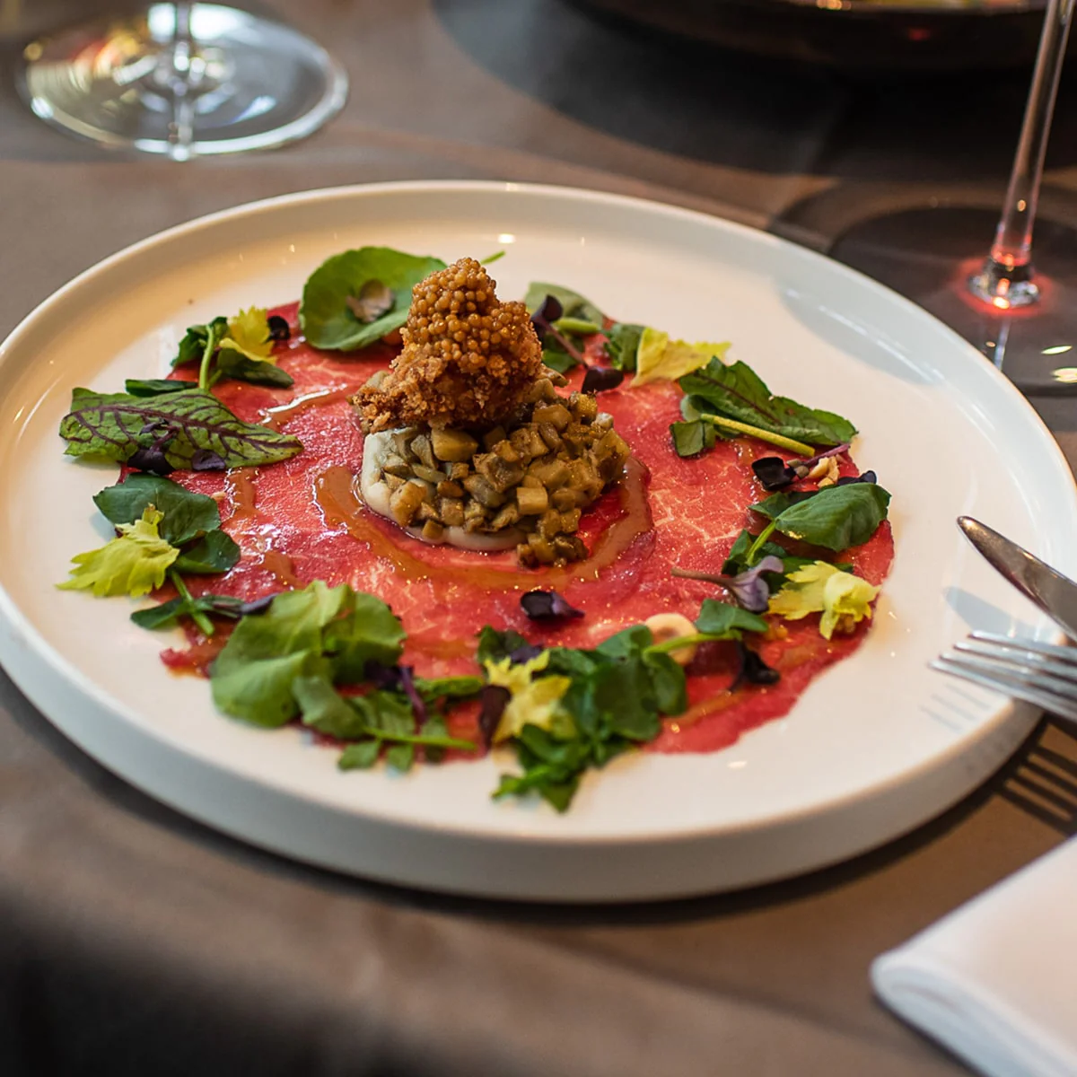 A gourmet dish with raw meat, diced vegetables, and greens on a white plate.