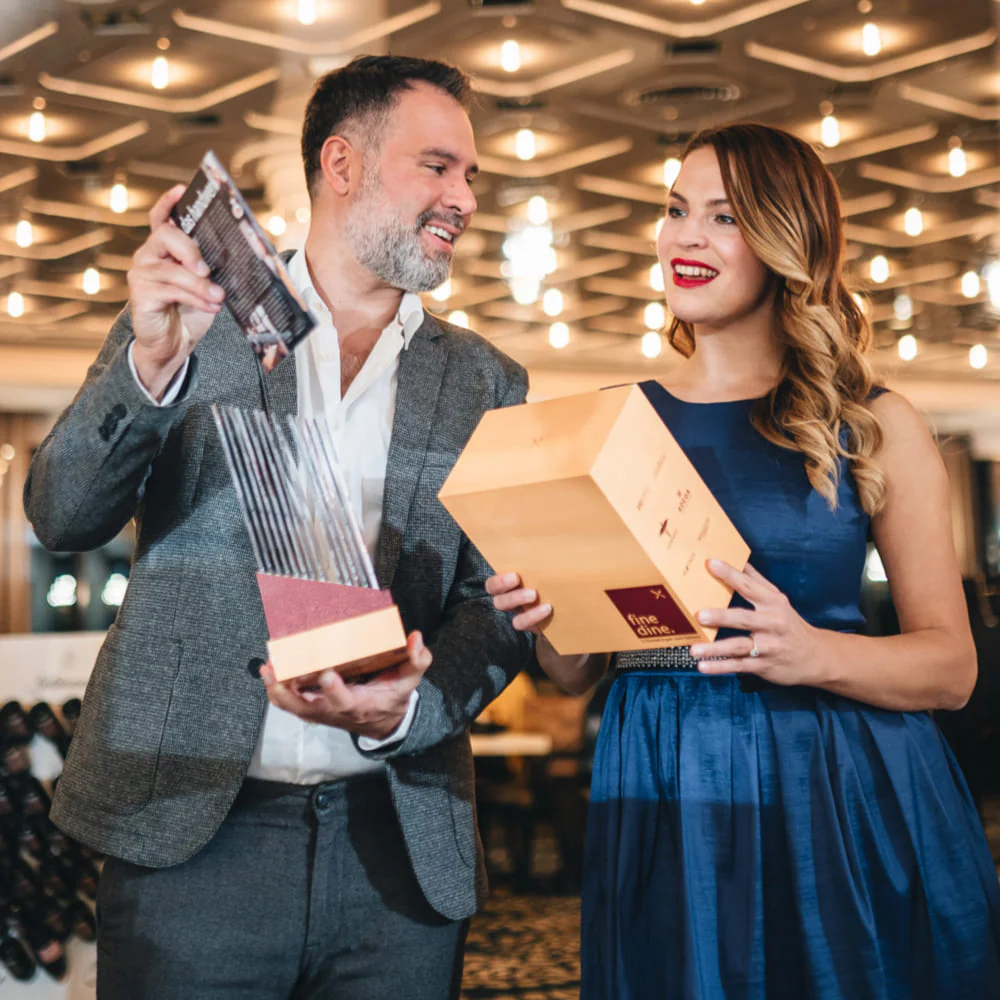 Two people smiling while holding an award and a box.