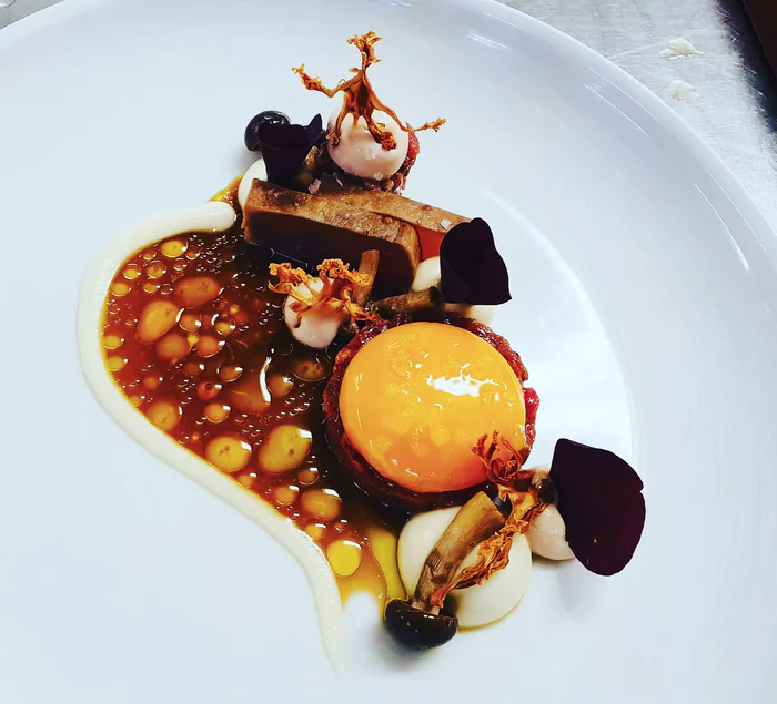Gourmet dish with various textures, sauces, and decorative elements on a white plate.