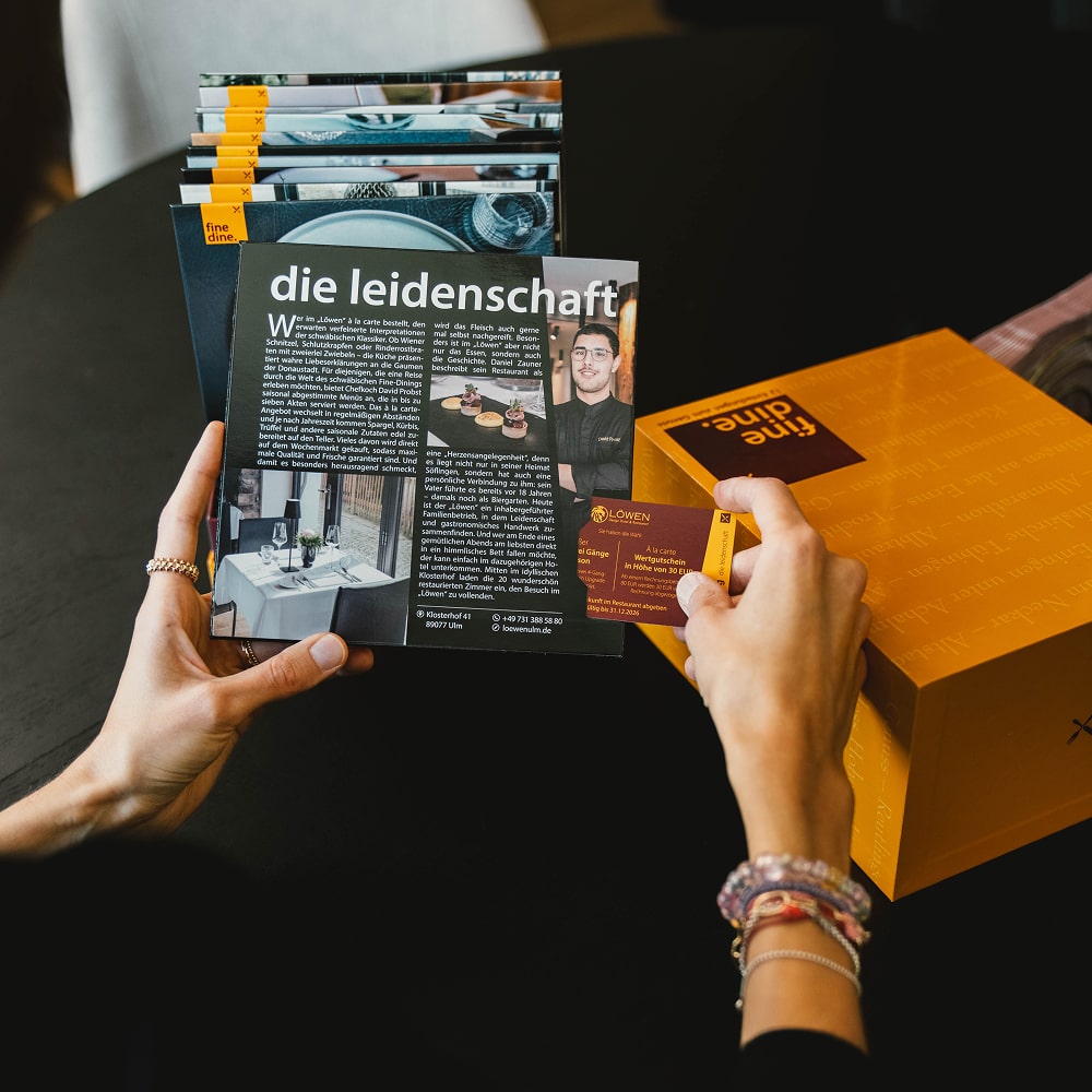 Person holding a magazine page and business card over a table.
