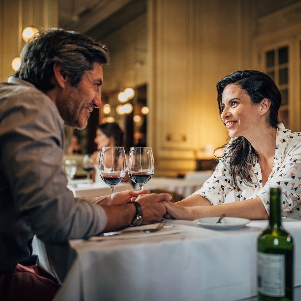 A couple holding hands at a restaurant table with wine glasses.