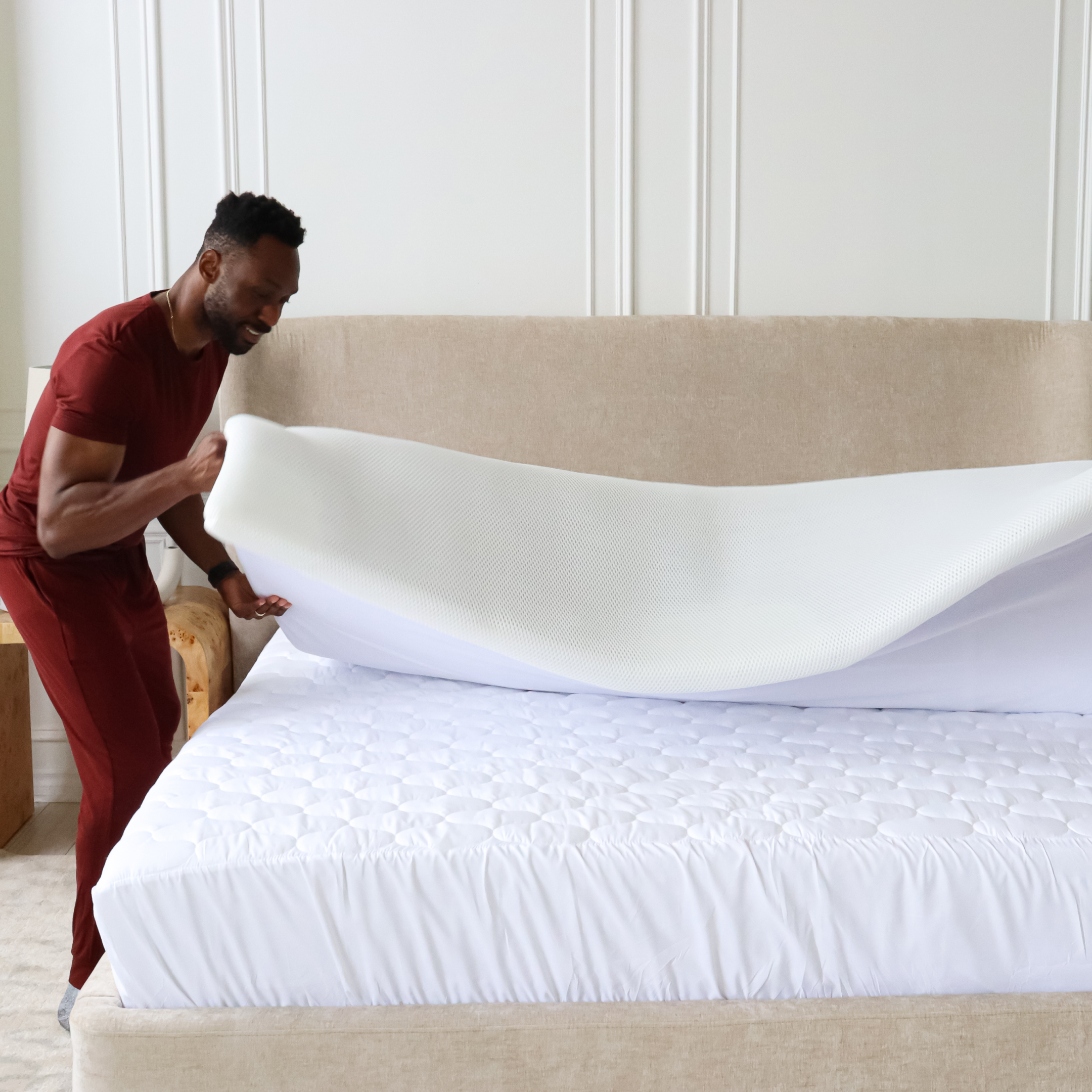 Person fitting a mattress protector on a bed in a bright room.
