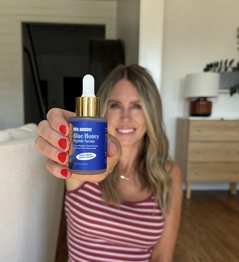 A woman with red nail polish holds a bottle of Evil Goods! Blue Honey Peptide Serum.