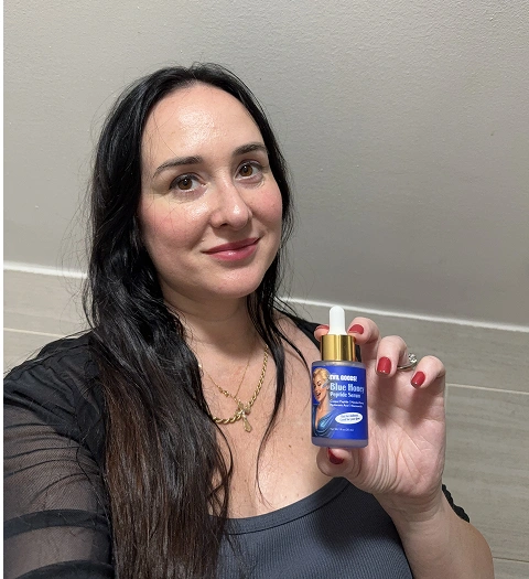 A woman with long dark hair holds up a small blue bottle of skincare serum.