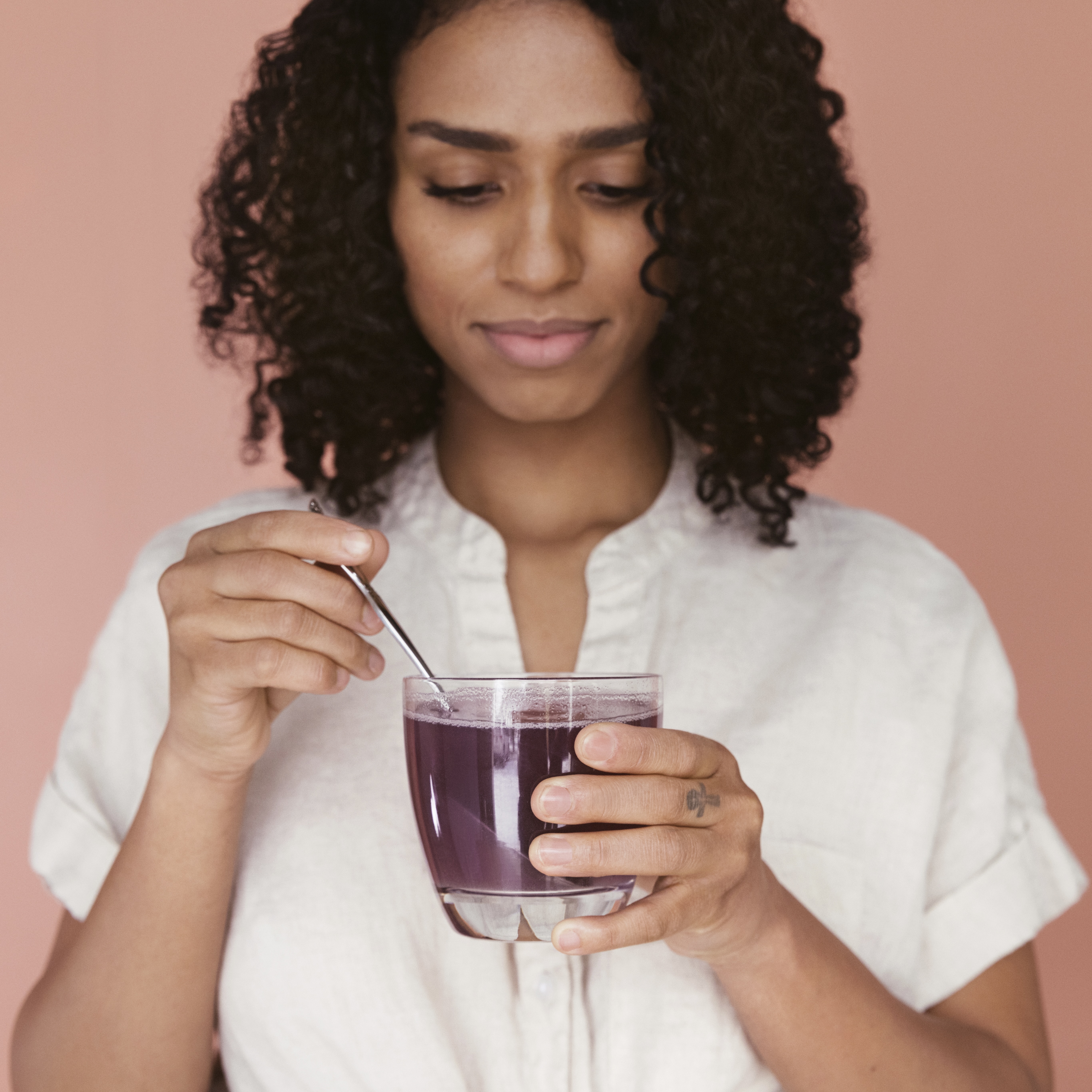 Person stirring a purple drink in a glass with a spoon.