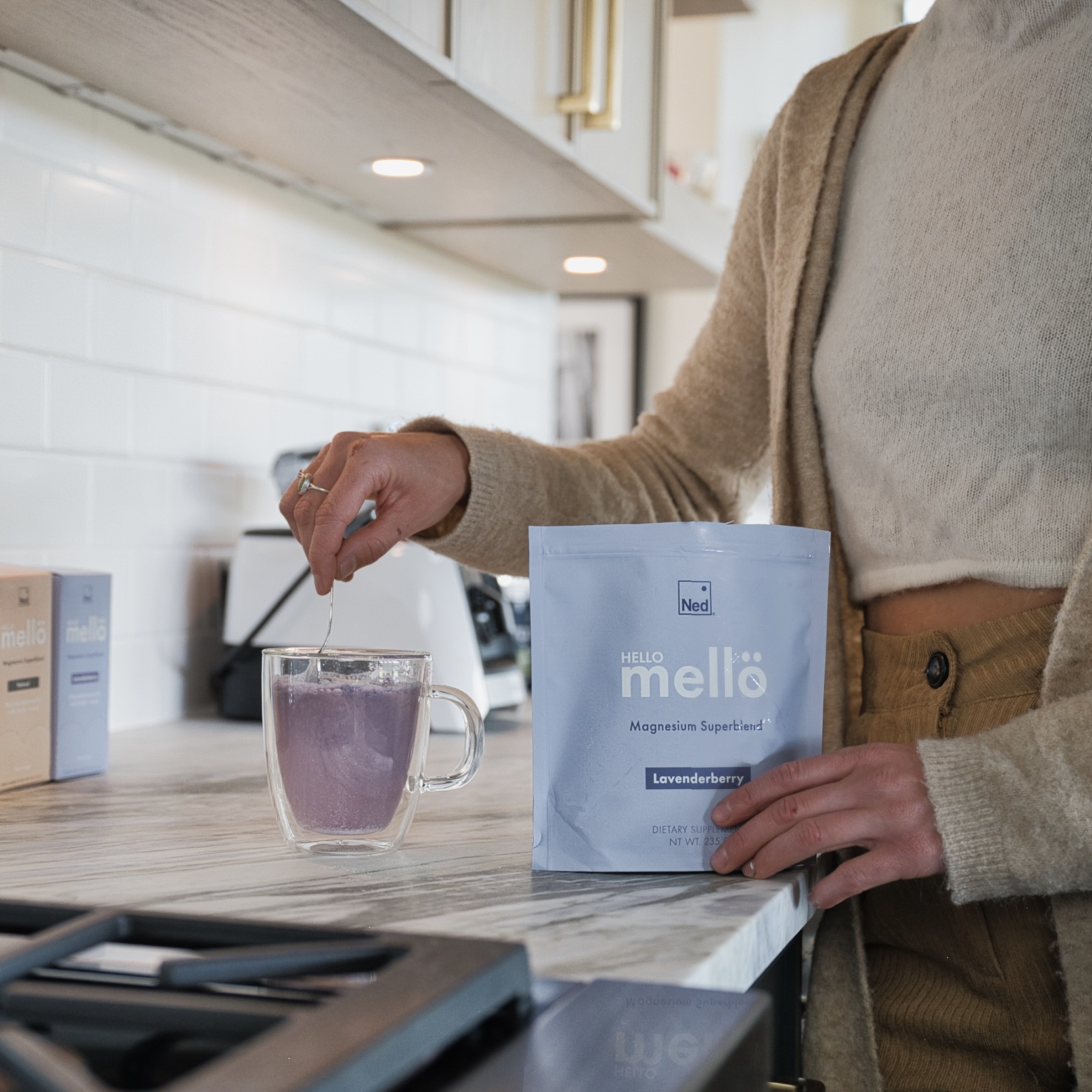 Person stirring a purple drink in a kitchen with a supplement packet.