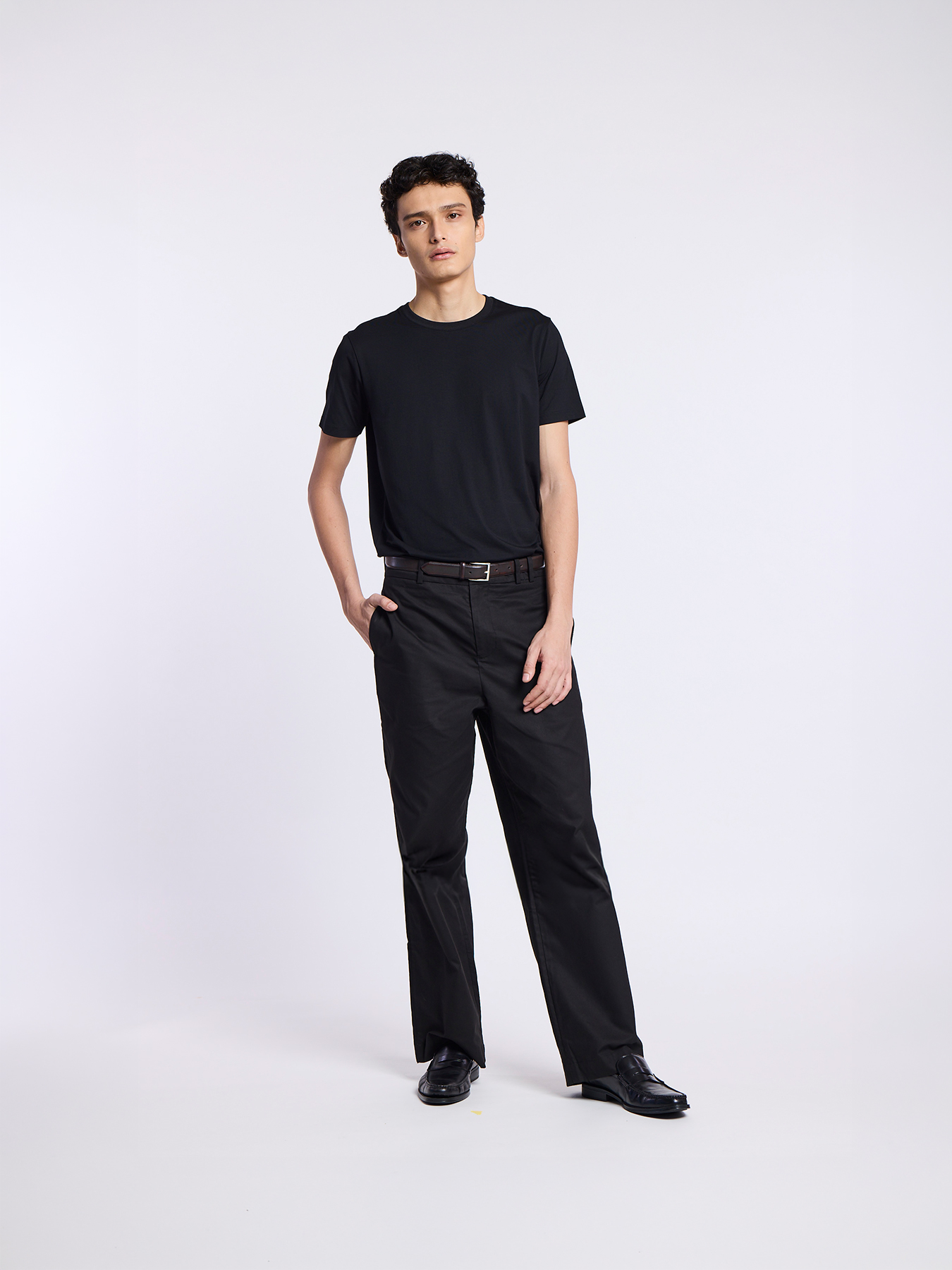 A man wearing a black t-shirt and black pants poses against a white background.