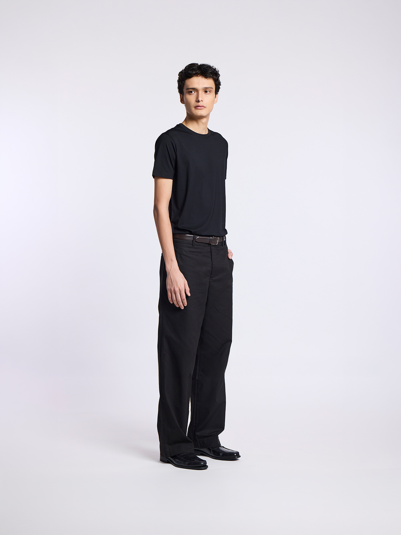 A man in a black t-shirt and black trousers poses against a plain white background.