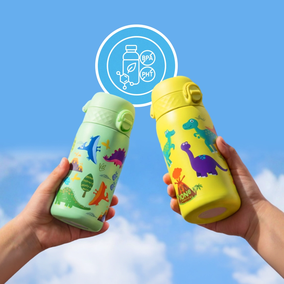 Two hands hold up green and yellow kids' water bottles with dinosaur designs against a blue sky.