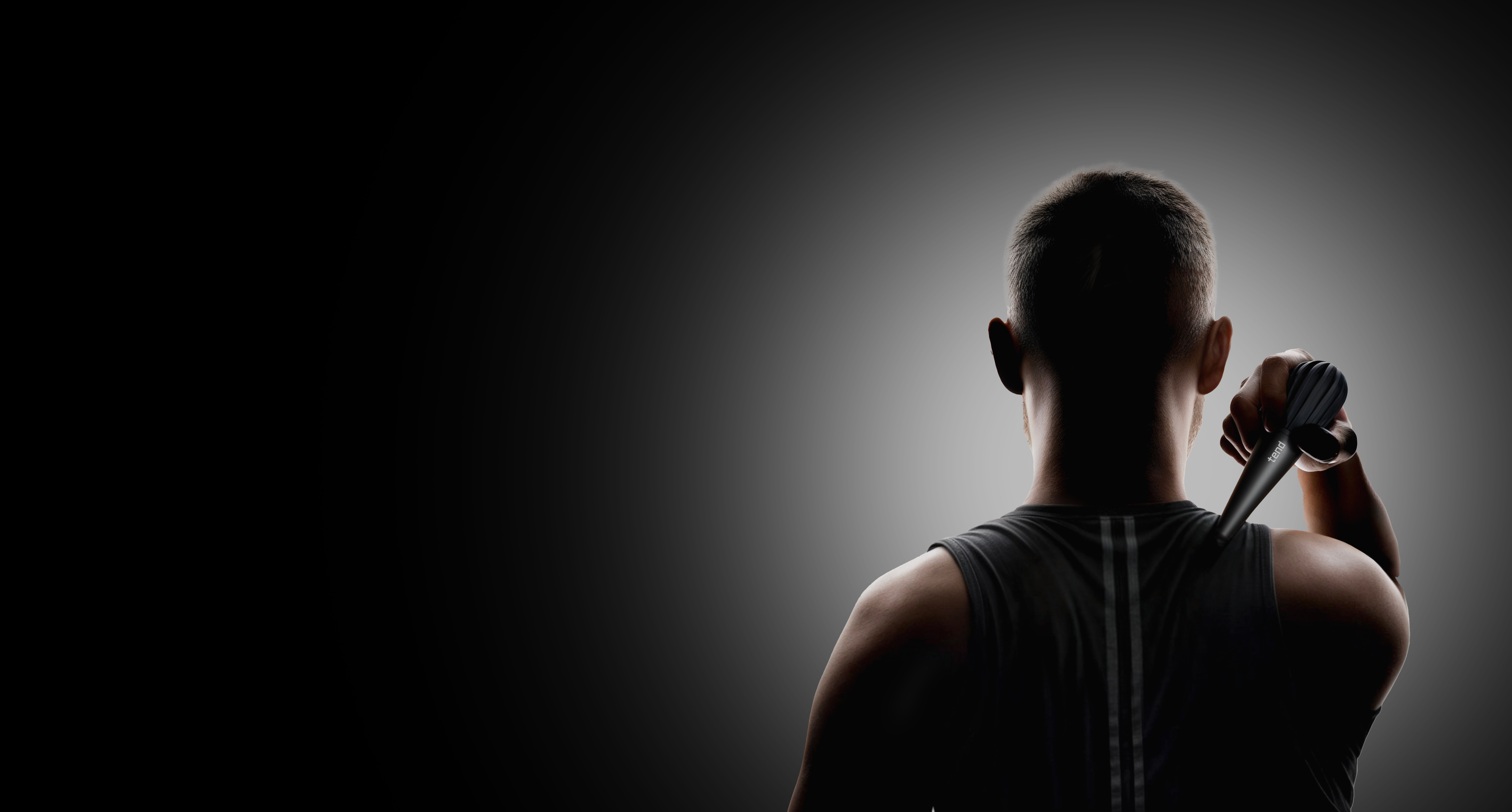 Person using a massage device on their back, dark background.