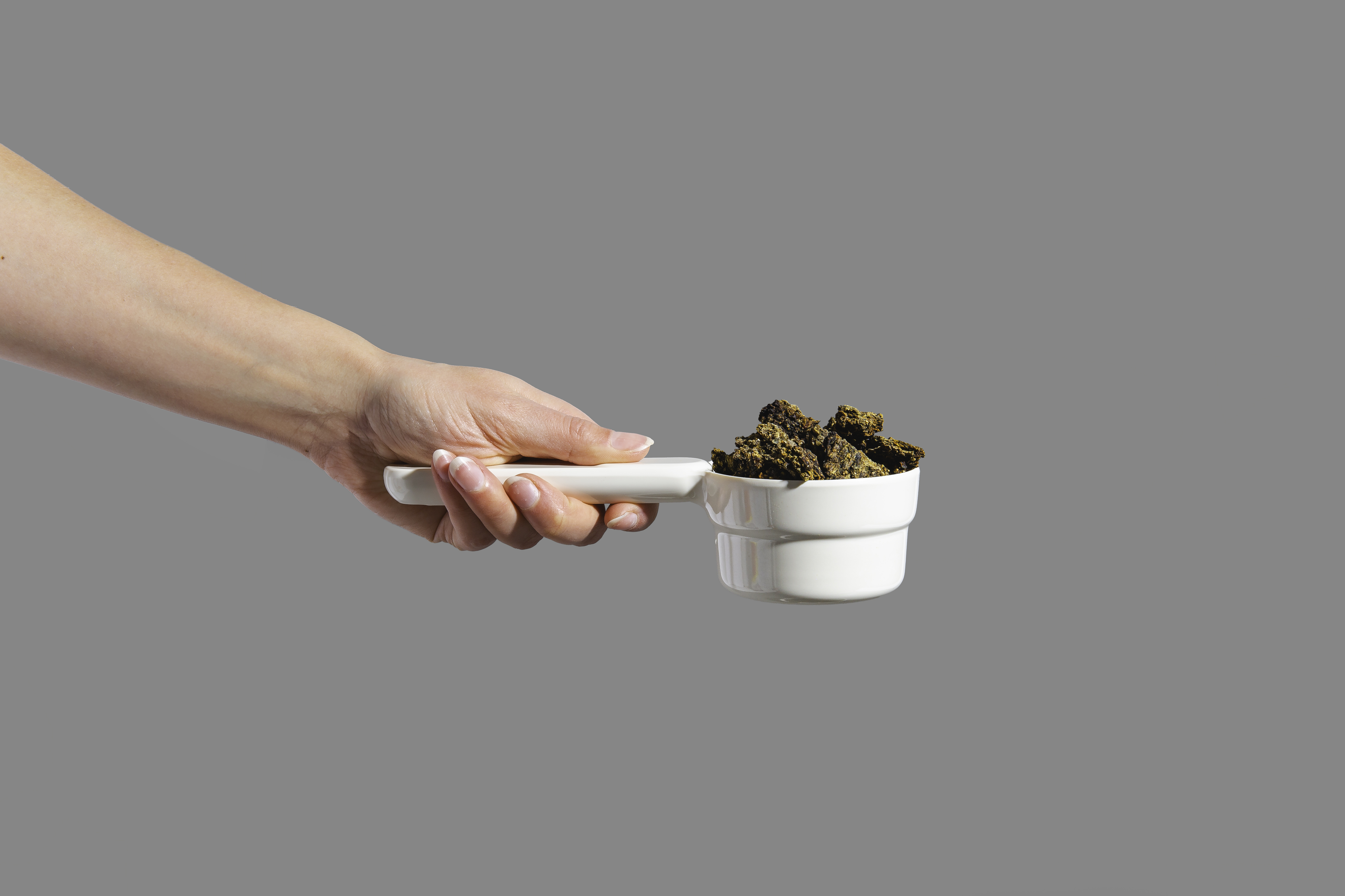 Hand holding a white measuring cup with dark brown chunks.