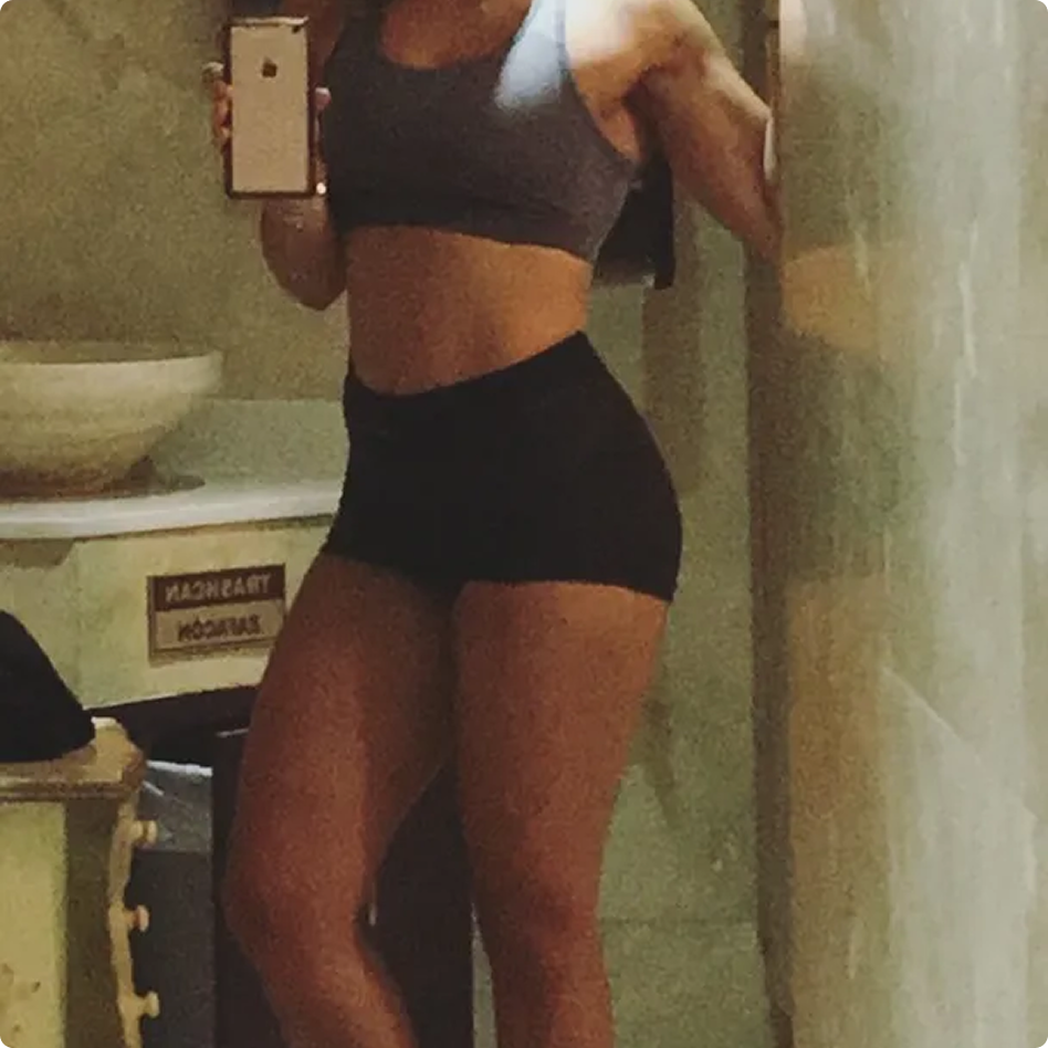 A fit person in a sports bra and shorts takes a mirror selfie with their phone.