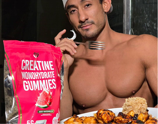 A shirtless, muscular man with a plate of food and a bag of creatine monohydrate gummies.