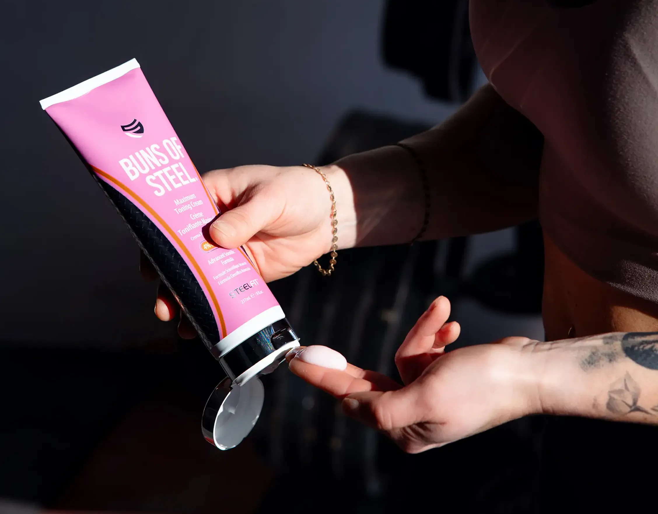 A person squeezes a small amount of Buns of Steel toning cream from a pink tube onto their finger.