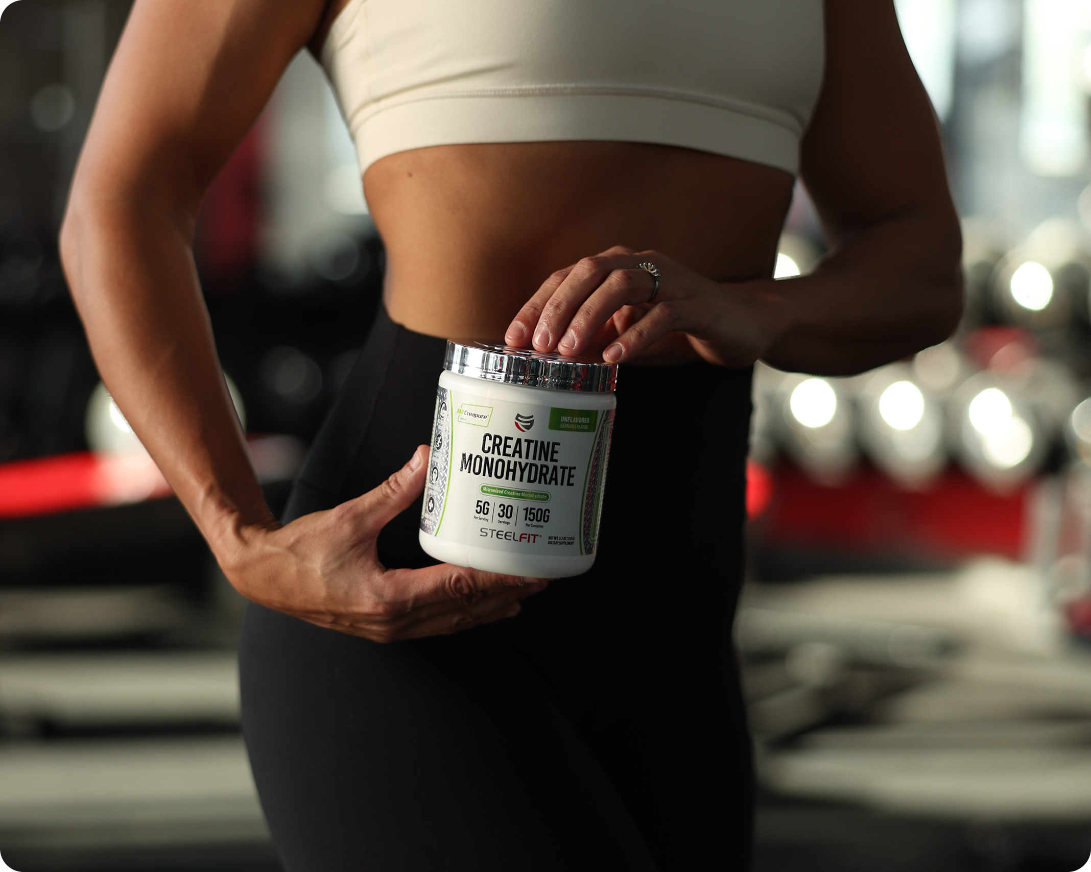 A close-up of a fit woman in a gym holding a tub of Steelfit Creatine Monohydrate.