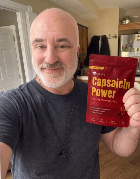 A smiling, bald man with a gray beard holds up a red pouch of Capsaicin Power supplements.