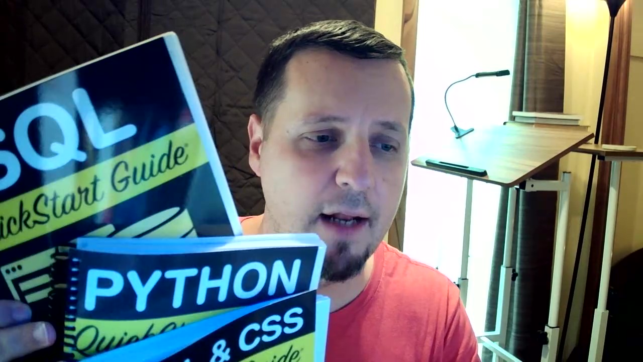 Person holding SQL, Python, and CSS guidebooks in a room with a desk and lamp.