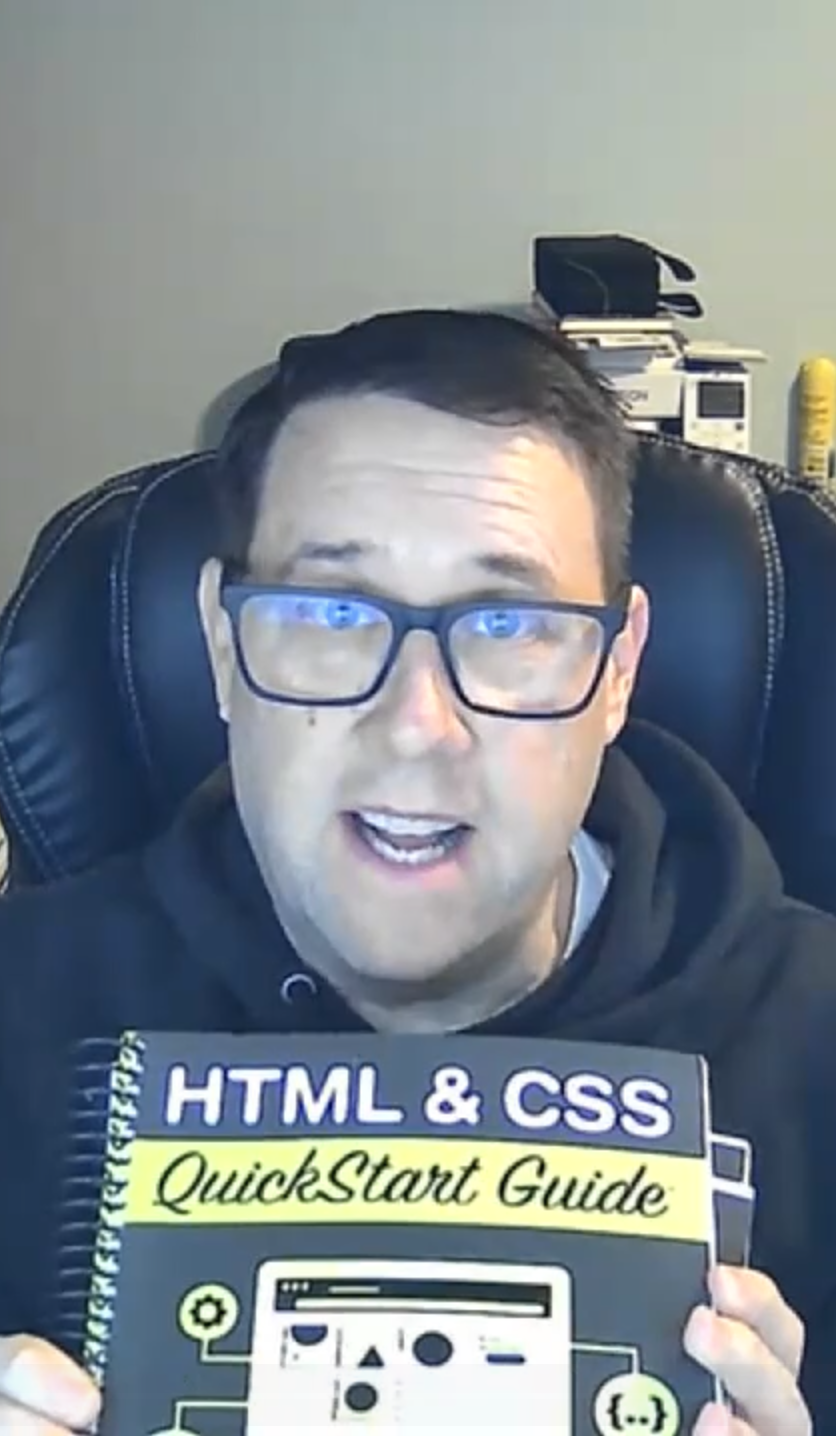 Person holding an 'HTML & CSS QuickStart Guide' book, sitting in a chair.