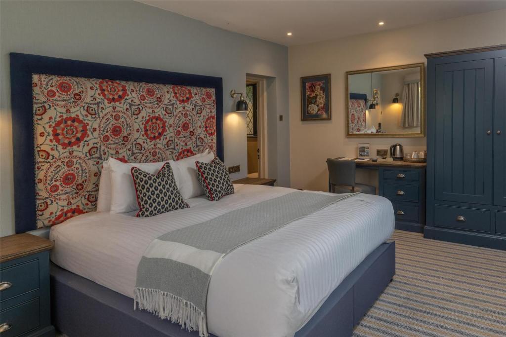 A hotel bedroom with a large bed featuring a colorful patterned headboard and blue wooden furniture.