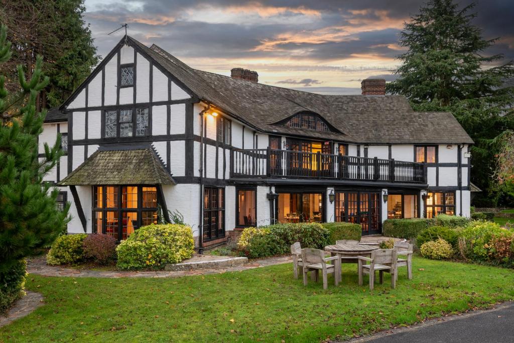 A large, black and white Tudor-style house with a front lawn and trees at dusk.