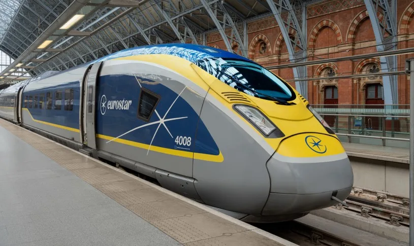 A blue, yellow, and grey Eurostar train waiting at a platform in a large train station.