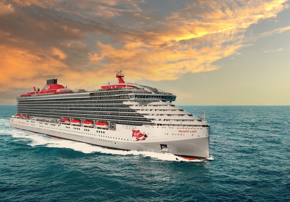 The Virgin Voyages cruise ship, Valiant Lady, sailing on the ocean under a colorful, cloudy sky.