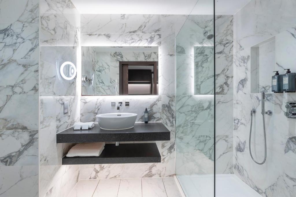 A modern bathroom with white marble walls, a black floating vanity, and a glass walk-in shower.